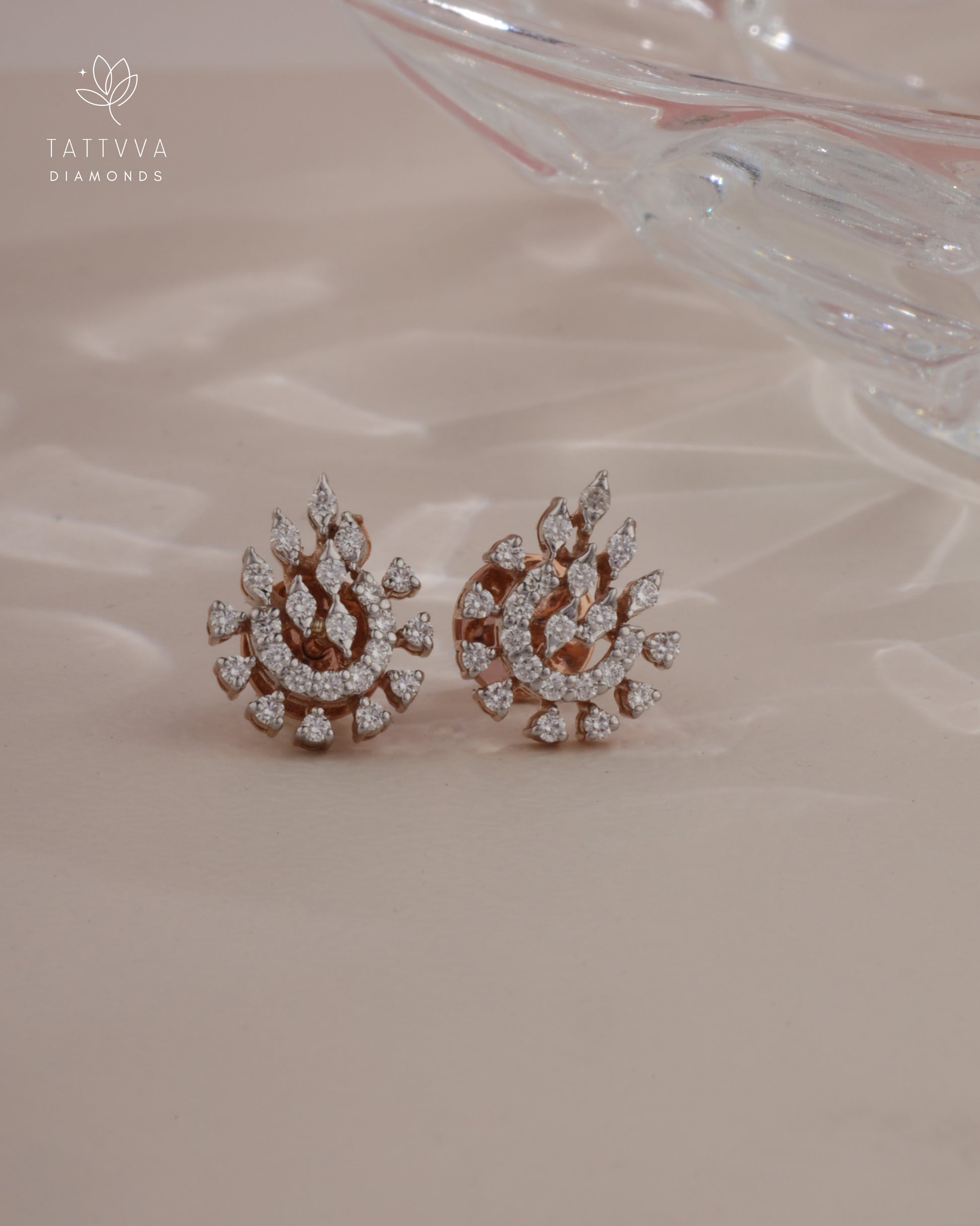 Pair of diamond earrings on a soft pink background with Tattvva Diamonds logo.