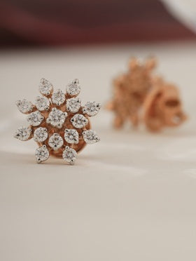 Rose gold earrings with diamond-like stones on a light background