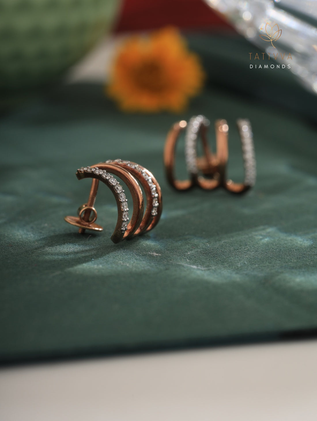 Rose gold hoop earrings with diamonds on a green surface