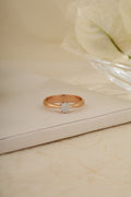 Rose gold ring with a diamond on a beige surface
