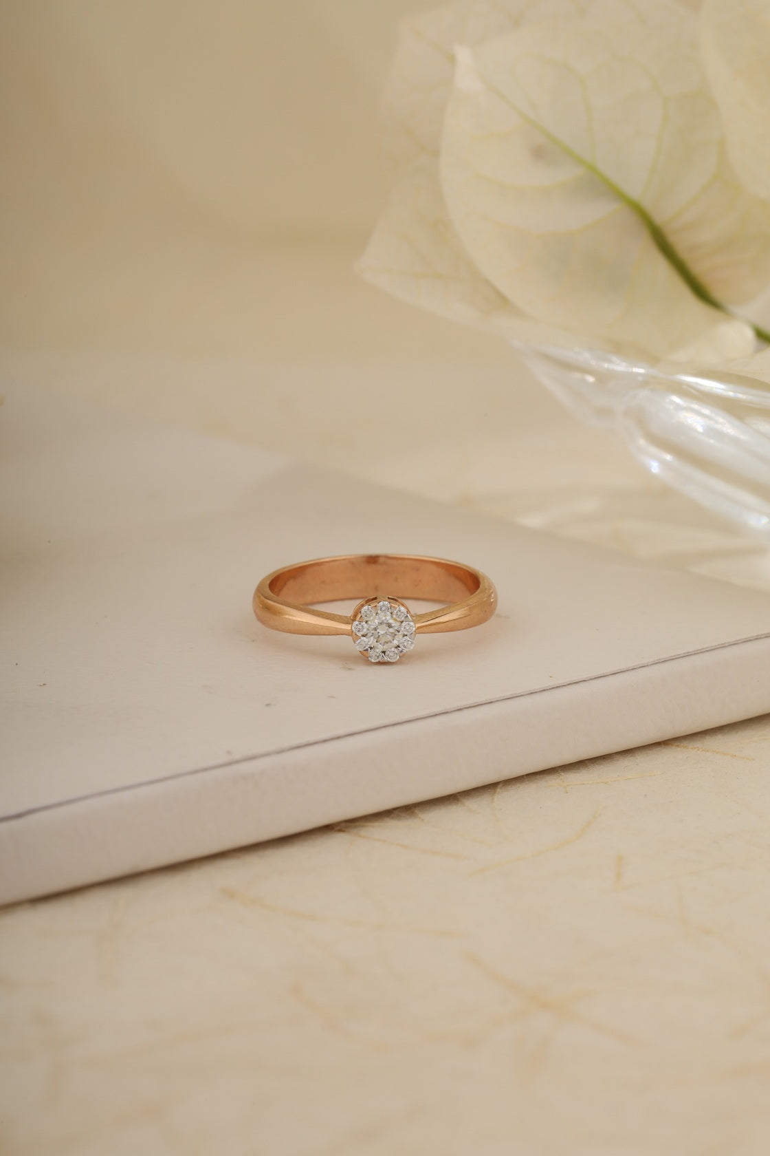 Rose gold ring with a diamond on a beige surface