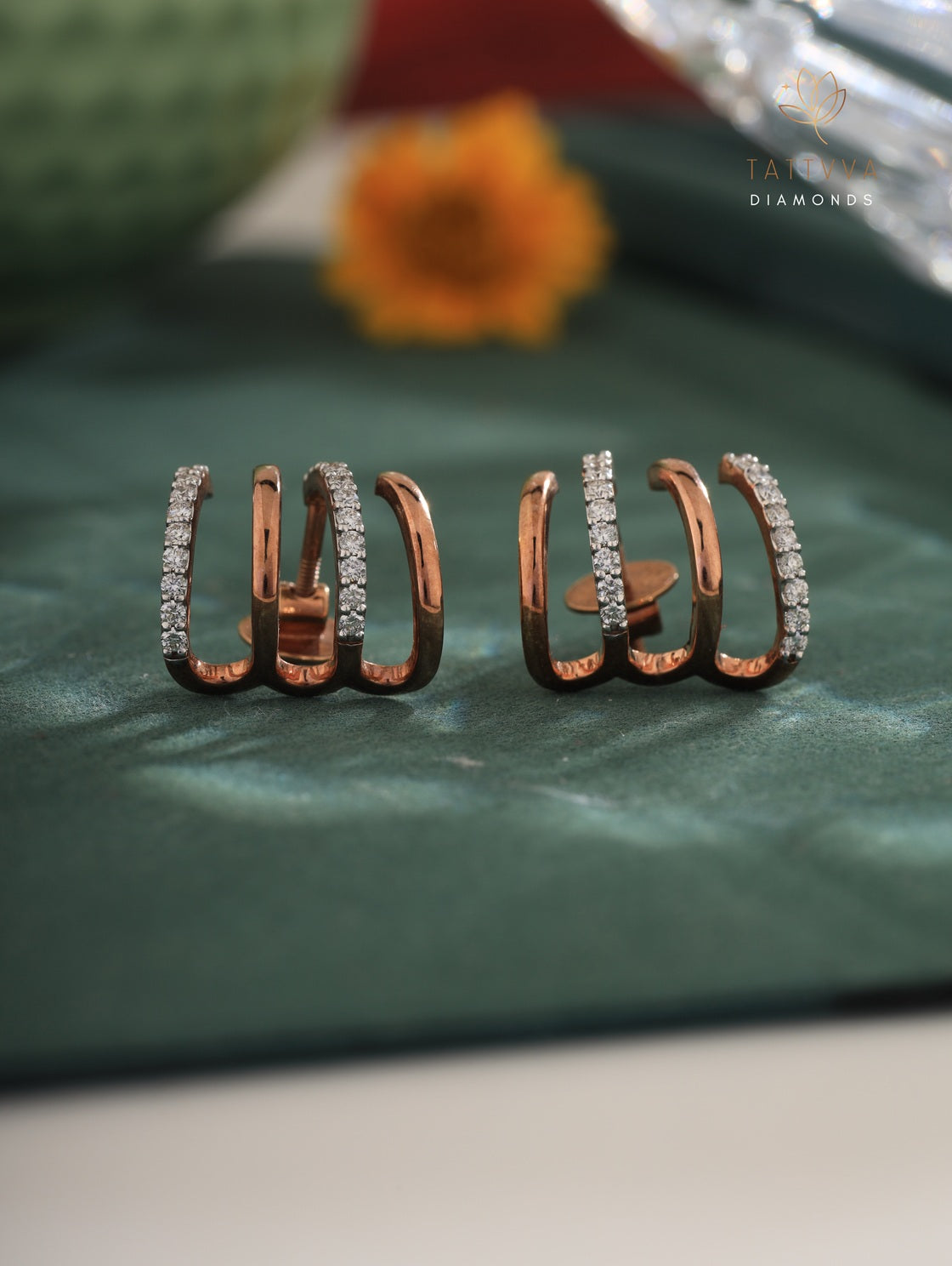 Rose gold hoop earrings with diamonds on a green surface