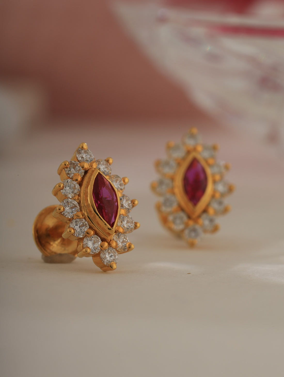 Gold earrings with red gemstones and clear stones on a light background