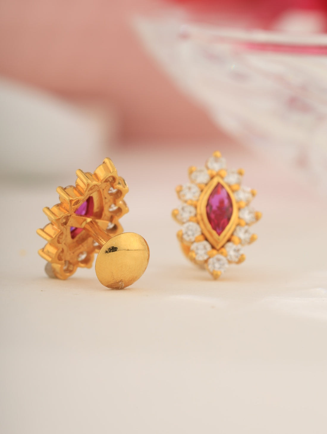 Gold earrings with red gemstones and clear stones on a light background