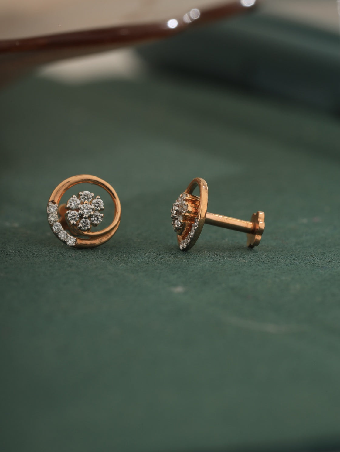 Pair of gold earrings with diamond-like stones on a green surface