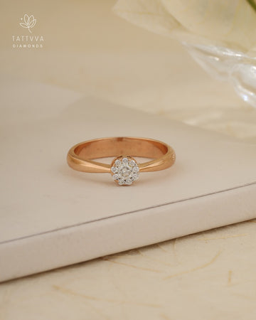 Rose gold ring with a diamond on a beige surface, branded 'Tattvva Diamonds'.
