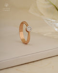 Rose gold ring with a diamond on a beige surface, featuring Tattvva Diamonds branding.