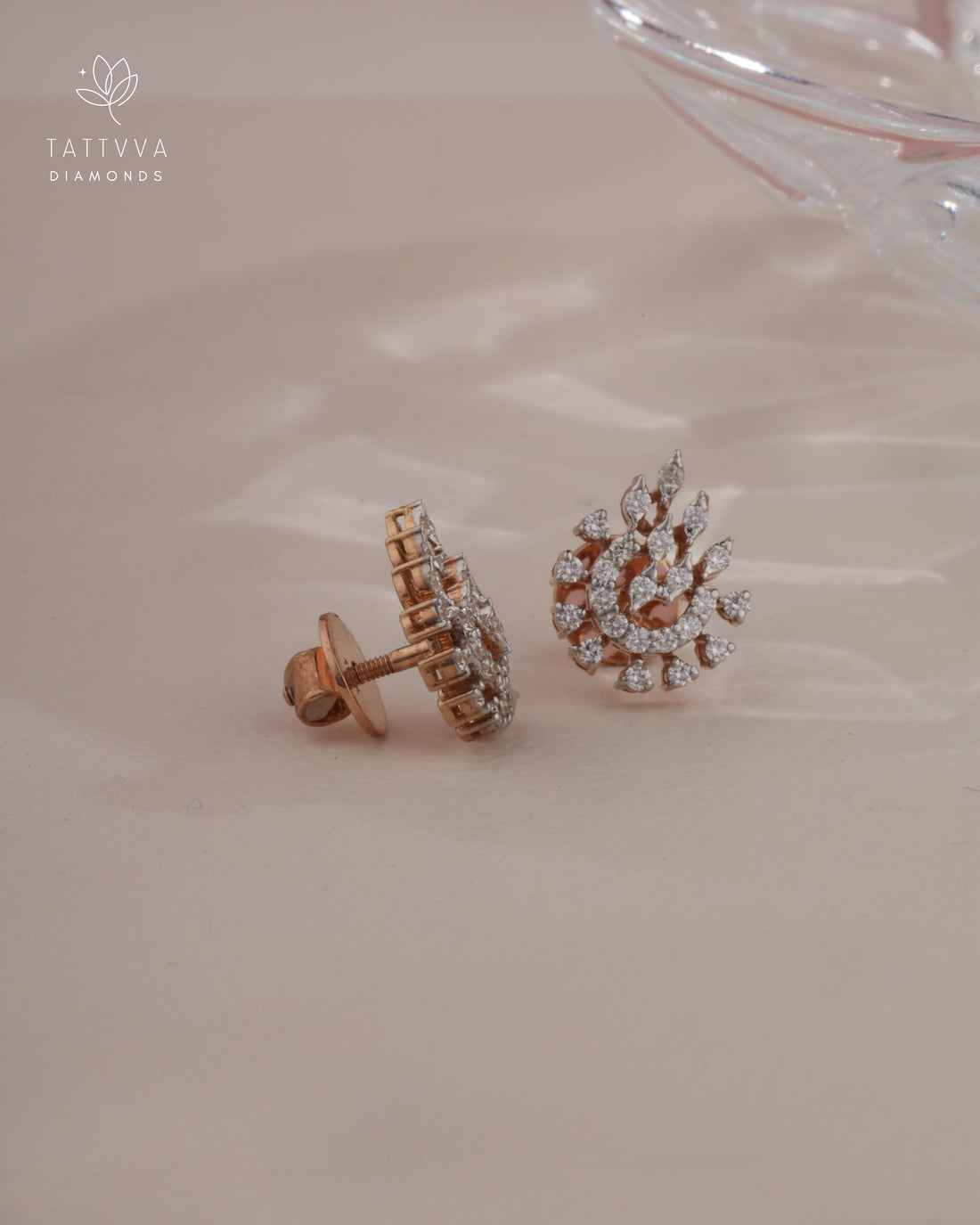 Pair of diamond earrings on a soft pink background with Tattvva Diamonds logo.
