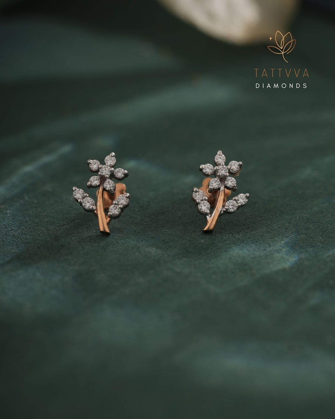 Pair of diamond earrings on a green leaf background with Tattvva Diamonds logo.