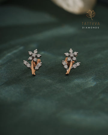 Pair of diamond earrings on a green leaf background with Tattvva Diamonds logo.