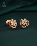 Rose gold floral earrings with diamonds on a dark green fabric background, featuring the Tattvva Diamonds brand.